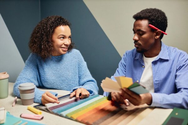Smiling Female Designer Working with Colleague Selecting Color of Fabric at Table